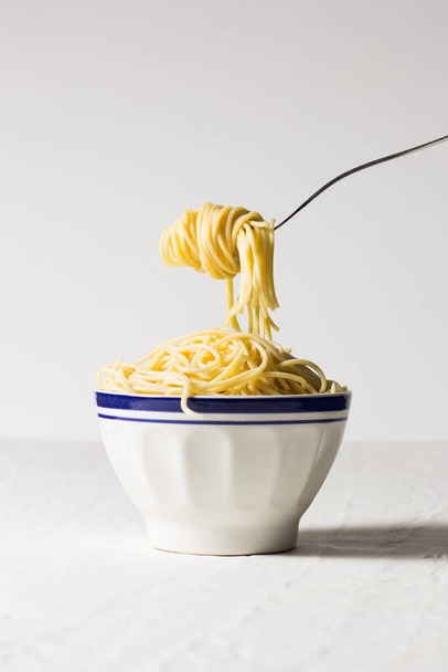Вилка со спагетти, подвешенной над миской, полной спагетти.. - Фото, изображение