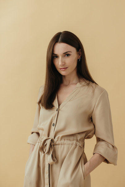 Ritratto di una bella bruna elegante in un abito lungo su sfondo beige. - Foto, immagini