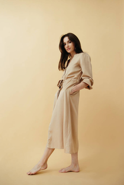 Portrait of a beautiful elegant brunette in a long dress on a beige background. - Photo, Image