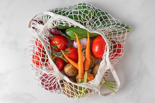 Organic vegetables in reusable shopping mesh bag or string bag from the market on white background. Top view. Eco friendly, zero waste concept - Foto, afbeelding