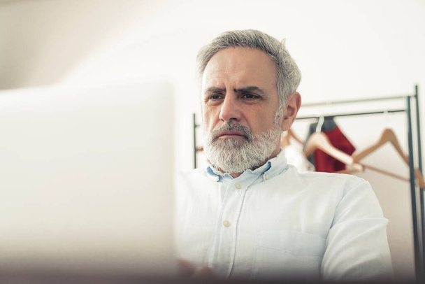 Der grauhaarige, bärtige Unternehmer arbeitet an seinem Laptop. Ein fokussierter Mann mittleren Alters. Hochwertiges Foto - Foto, Bild