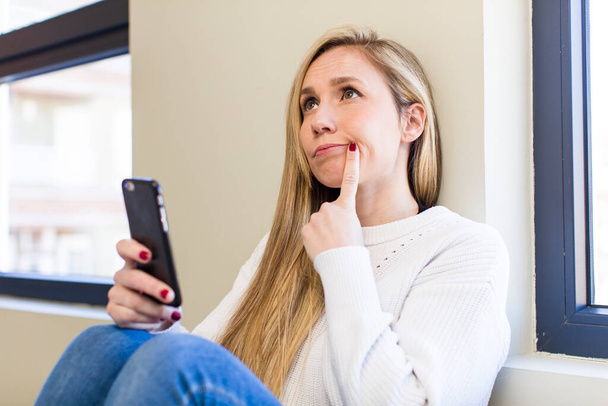 young adult pretty blonde woman using her smartphone at home - Foto, Bild