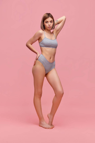 Portrait of young thin sportive woman in grey cotton inner wear posing over pink background. Concept of natural beauty, body and skin care, health, anti-cellulite program, ad. - Fotoğraf, Görsel