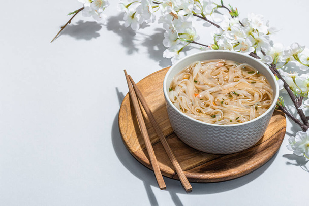 Korean noodles Ramen with broth. Hot dish, chopsticks, hard light, dark shadow. Gray background, cherry flowers, flat lay, copy space - Valokuva, kuva