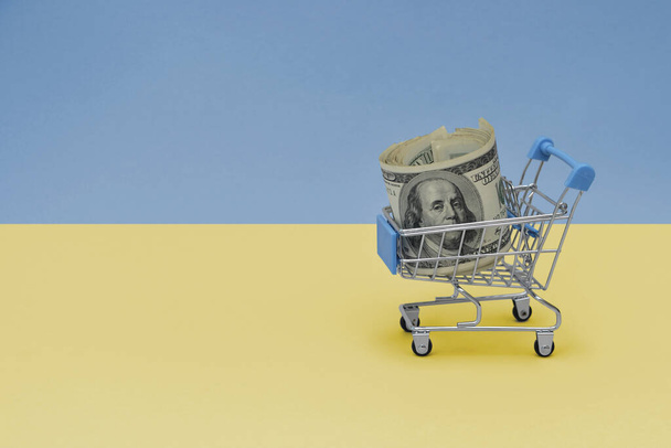 Cesta de la compra del metal con el billete de dinero del dólar grande en la bandera nacional del fondo ucraniano. concepto de cesta de consumo. ilustración 3d - Foto, imagen