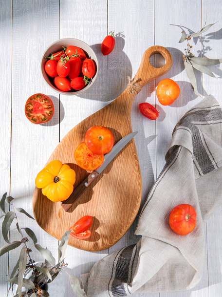 Gesorteerde tomaten op een houten keukenbord. Kleurrijke tomaten van verschillende rassen en kleuren. Biologische en verse groenten uit de tuin. Bovenaanzicht - Foto, afbeelding