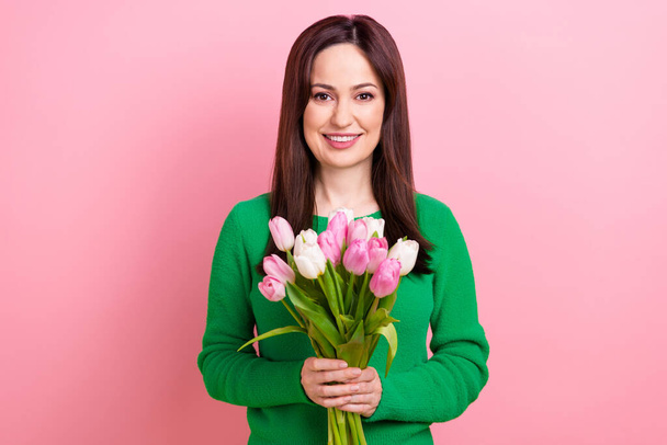 Photo of pretty charming woman wear green smiling holding tulips bouquet isolated pink color background. - Foto, immagini