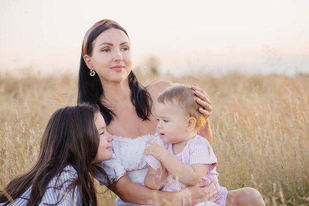happy mom with two little daughters on summer field at sunset - Foto, imagen