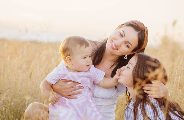 happy mom with two little daughters on summer field at sunset - Photo, image