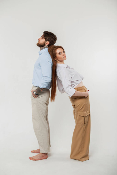 Beautiful young fashionable business couple man and woman in an elegant stylish vintage clothing with shirt and pants standing back to back on a white background - Photo, image
