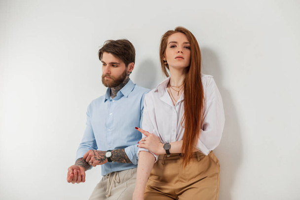 Fashionable beautiful young couple on a white background. Beautiful elegant redhead woman model and fashion handsome brutal hipster man with tattoo and beard in shirt - Фото, изображение