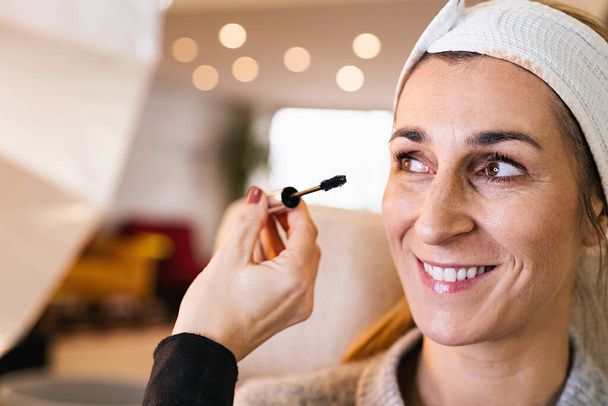 make-up assistent aanbrengen make-up tot wimpers van een gelukkig model voor een fotoshoot op locatie. - Foto, afbeelding