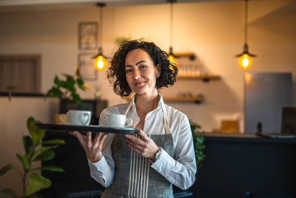 One mature woman caucasian waitress at cafe or restaurant carry tray with coffee female entrepreneur at work real people copy space small business concept - Foto, imagen