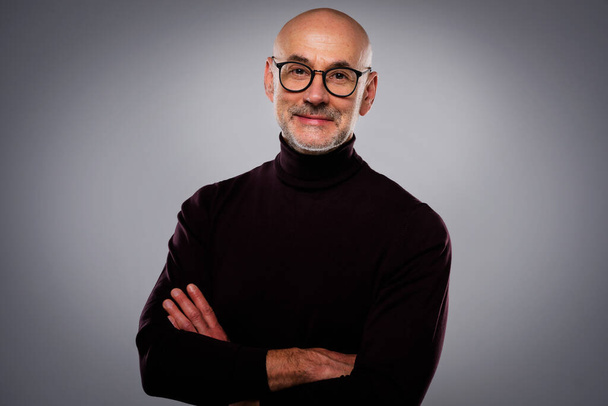 Close-up studio portrait of confident man standing at isolated grey background. Smiling male wearing eyewear and turtleneck sweater. Copy space.  - Fotoğraf, Görsel