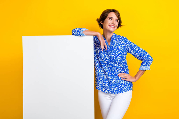 Photo of adorable dreamy woman dressed blue blouse holding empty space placard isolated yellow color background. - Foto, Imagen