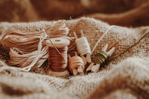 Dikiş nakış seti. Eski kumaş çuval bezinin arka planında iplikler, ahşap, halka - Fotoğraf, Görsel