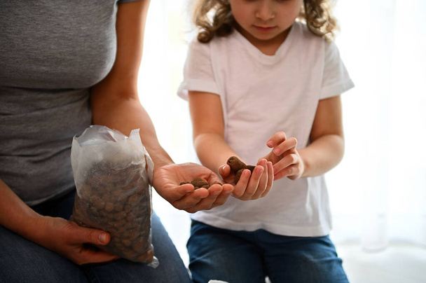 Selective focus on the hands of a little child girl holding expanded clay while helping her mom in planting houseplants. Floriculture. Horticulture. Agriculture. Gardening. Houseplant care concept - Photo, Image