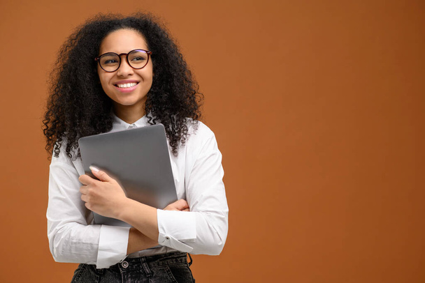 Nice pretty African american female student or coworker holding clutching laptop in anticipation new job or interesting tasks and smiling, female office employee in formal wear isolated on brown - Foto, immagini