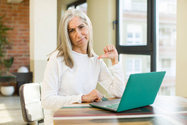 senior pretty woman feeling cross,showing thumbs down with a laptop - Photo, Image
