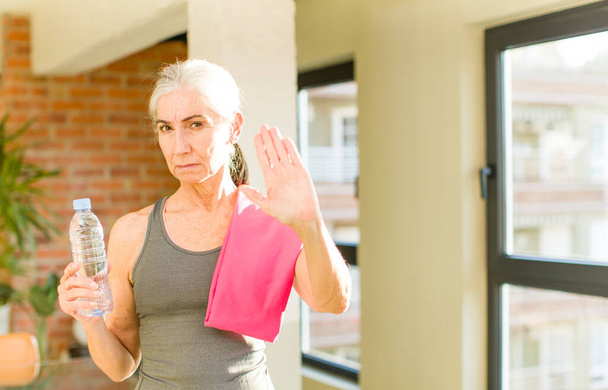 starší hezká žena, která vážně ukazuje otevřenou dlaň, aby zastavila gesto. fitness koncept - Fotografie, Obrázek