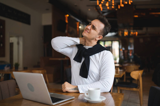 Egy férfi kaukázusi felnőtt férfi ül az asztalnál kávézó étteremben számítógép laptoppal böngészni az interneten, vagy a munka valós emberek másolja tér hold nyak fájdalommal hát- vagy nyaki feszítés - Fotó, kép