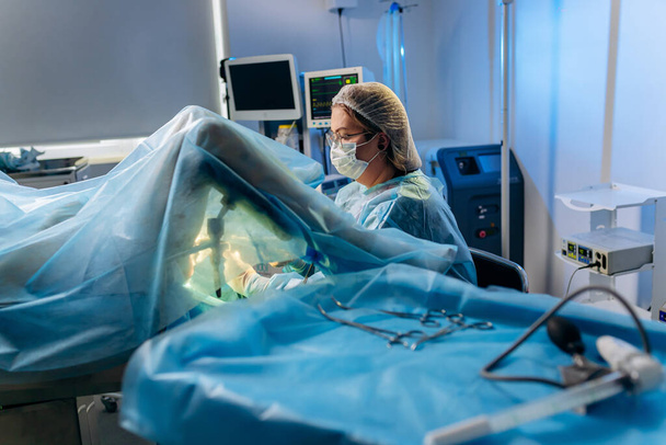 Chirurgienne proctologue professionnelle effectuant une opération à l'aide de dispositifs médicaux spéciaux dans la salle d'opération de l'hôpital. Concept chirurgical urgent - Photo, image