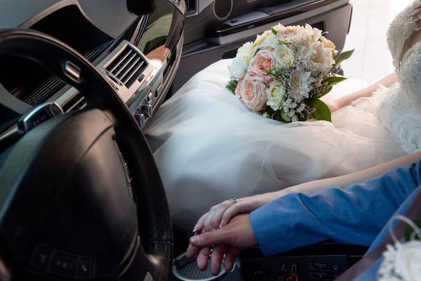 τα χέρια της νύφης και του γαμπρού με ένα μπουκέτο στο αυτοκίνητο στο γάμο - Φωτογραφία, εικόνα