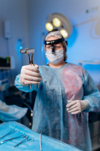 A female surgeon in the operating room holds an anus dilator. A doctor in a medical mask prepares medical instruments for coloproctological surgery - Фото, изображение