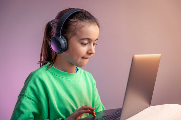 Funny little girl in headphones with laptop plays games, game addiction concept, copy space. - Foto, immagini