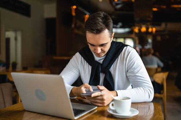 Jeden człowiek siedzi przy stole w kawiarni lub restauracji nosić casual za pomocą telefonu komórkowego do przeglądania Internetu lub wiadomości SMS komunikacji prawdziwi ludzie skopiować przestrzeń - Zdjęcie, obraz