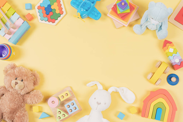 Baby kids toy frame background. Teddy bear, colorful wooden educational, musical, sensory, sorting and stacking toys for children on yellow background. Top view, flat lay. - Foto, immagini