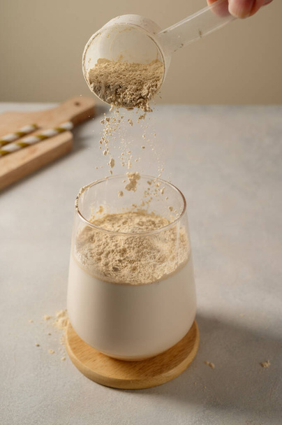 Pouring protein powder from scoop, in glass with milkshake - Foto, Bild