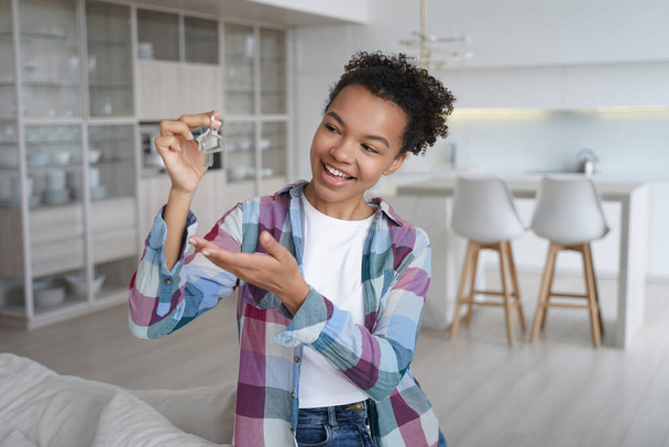 Joven mujer afroamericana alegre mostrando las llaves de la casa en un nuevo hogar. Biracial chica adolescente propietario, inquilino siente felicidad con la reubicación o la compra de piso. Alquiler de bienes raíces, primer apartamento propio. - Foto, Imagen
