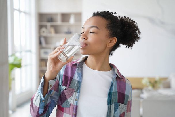 African american woman enjoy drinking pure crystal filtered potable water. Thirsty female with eyes closed swallow mineral aqua from glass at home kitchen. Thirst, healthy lifestyle, body care concept - Φωτογραφία, εικόνα