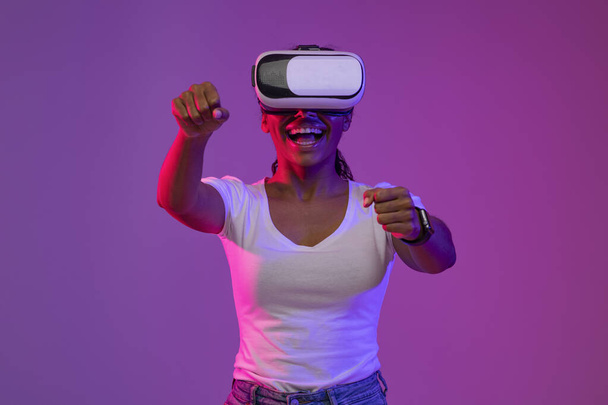 Happy Excited Black Woman Wearing VR Headset Experiencing Virtual Reality While Playing Online Game, Cheerful African American Lady Driving Imaginary Car, Holding Steering Wheel In Neon Light - Фото, зображення