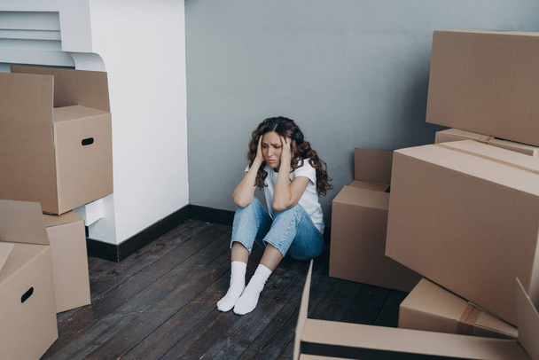 Unhappy hispanic woman packing boxes. Girl is frustrated with moving. Anxious young lady is sitting on the floor going to relocate. Mortgage debt and bankruptcy concept. - Photo, image