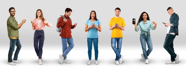 Smiling excited millennial different men and women in casual show smart phone with empty screen, chatting on white background, studio, panorama, full length. Modern device, app, great news and sale - Photo, Image