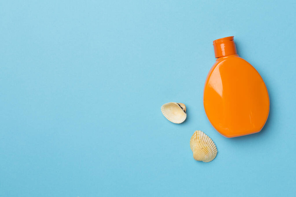 Bottle with sun protection cream and sea shells on wooden background, top view. - 写真・画像