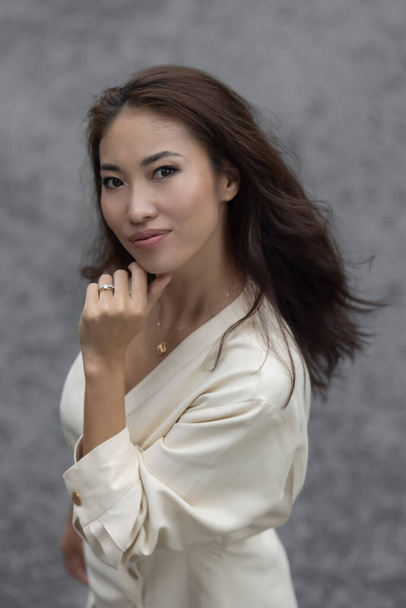Egy gyönyörű ázsiai lány fekete hajjal fehér ruhában Női vonzerő. Egy esztétikailag kellemes arcszerkezettel rendelkező személy. Egy modell smink és frizura. - Igen. Kiváló minőségű fénykép - Fotó, kép