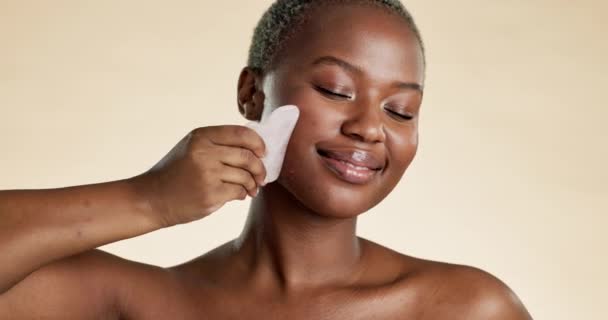 Black woman, face and facial gua sha, beauty and skincare, content and exfoliate, cosmetics tools on studio background. Healthy skin, glow and eyes closed, peace and female hand with cosmetic care. - Filmati, video