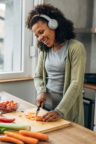 Vrolijke gemengde ras vrouw bereidt groenten voor het koken - Foto, afbeelding