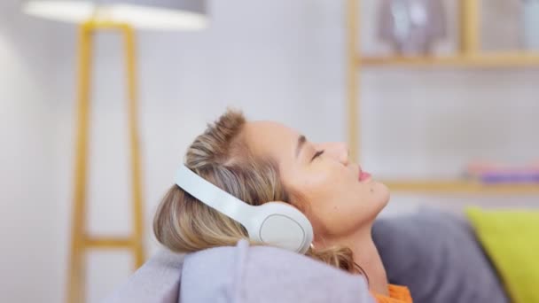 Relax, music headphones and woman on sofa in home living room streaming audio. Meditation, technology and young female on couch in lounge listening to peaceful podcast, radio song or sound in house - Video