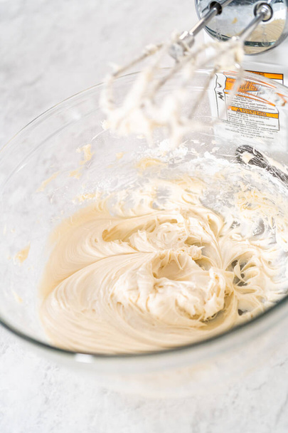 Misturar ingredientes com um misturador de mão em uma tigela grande para fazer cobertura de queijo creme para bolo de pacote de cenoura. - Foto, Imagem