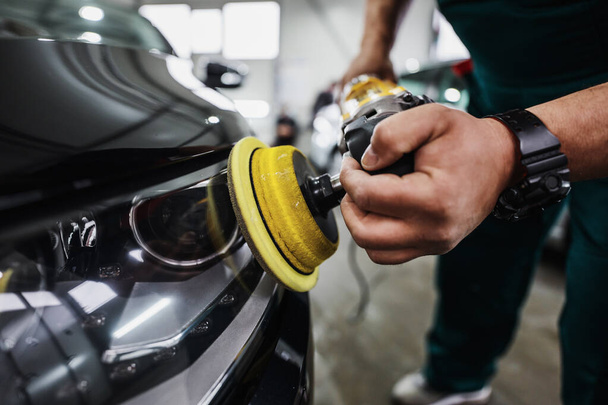 Professional car service worker polishing luxury car with orbital polisher in a car detailing and valeting shop. Ultra wide angle shot. - Фото, изображение