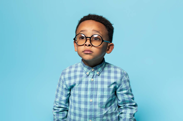Näkökyky. Muotokuva musta pieni poika silmälasit ja etsivät huolellisesti, poseeraa sininen studio tausta. Lasten silmät terveys ja näkö korjaus käsite - Valokuva, kuva
