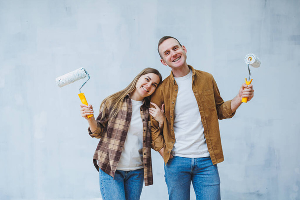 Una joven pareja de enamorados pinta las paredes con pintura blanca usando rodillos. Renovación en el apartamento de una pareja feliz - Foto, Imagen