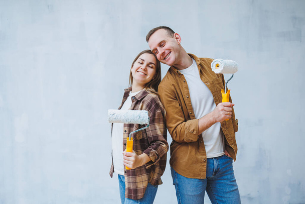 Um jovem casal apaixonado pinta as paredes com tinta branca usando rolos. Renovação no apartamento de um casal feliz - Foto, Imagem