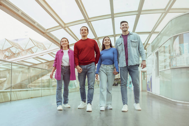 Tourism. Two Cheerful Couples Going On Vacation Together Walking Holding Hands In Modern Airport Indoors. Full Length Shot Of Group Of Four Young Tourists. Travel With Friends Concept - 写真・画像