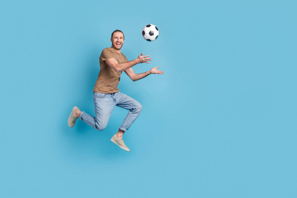 正の励起男の完全な長さの写真を着用ベージュtシャツジャンプ高演奏サッカー空のスペース隔離された青の色背景. - 写真・画像