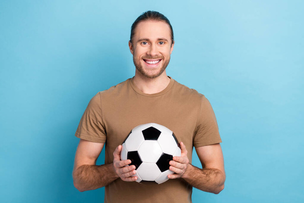 Photo of cheerful good mood man wear beige t-shirt holding football ball isolated blue color background. - Photo, Image